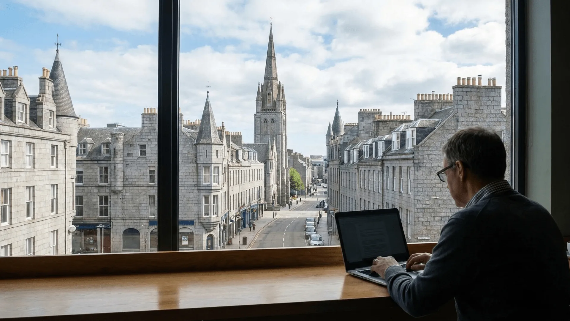 A GFX Computers customer working on a laptop by a window overlooking a granite street in Aberdeen