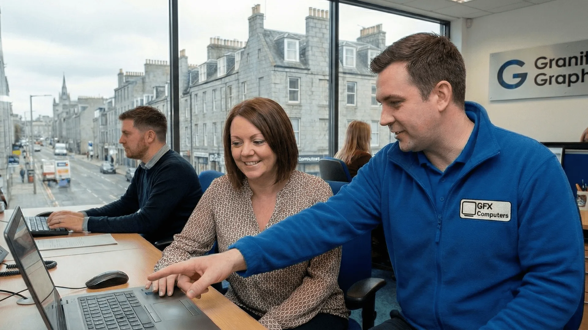 A GFX Computers engineer helping a small business owner at a laptop in an Aberdeen office